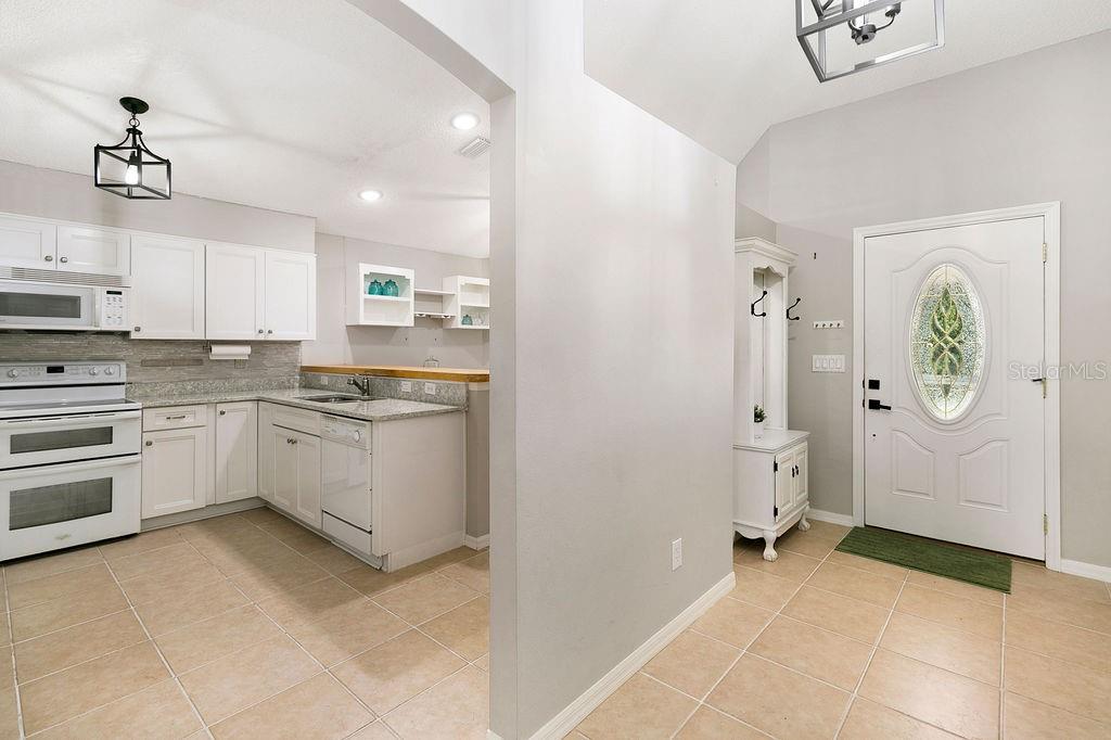 A kitchen with white cabinets and tile flooring sits adjacent to an entryway with a door — 4511 DERBYSHIRE DRIVE, TITUSVILLE, FL