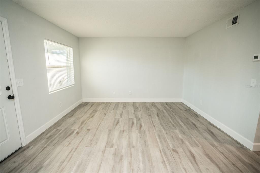 An empty room features light gray walls, wood-look flooring, and a single window with blinds — 11312 N 52ND STREET UNIT A11, TAMPA, FL
