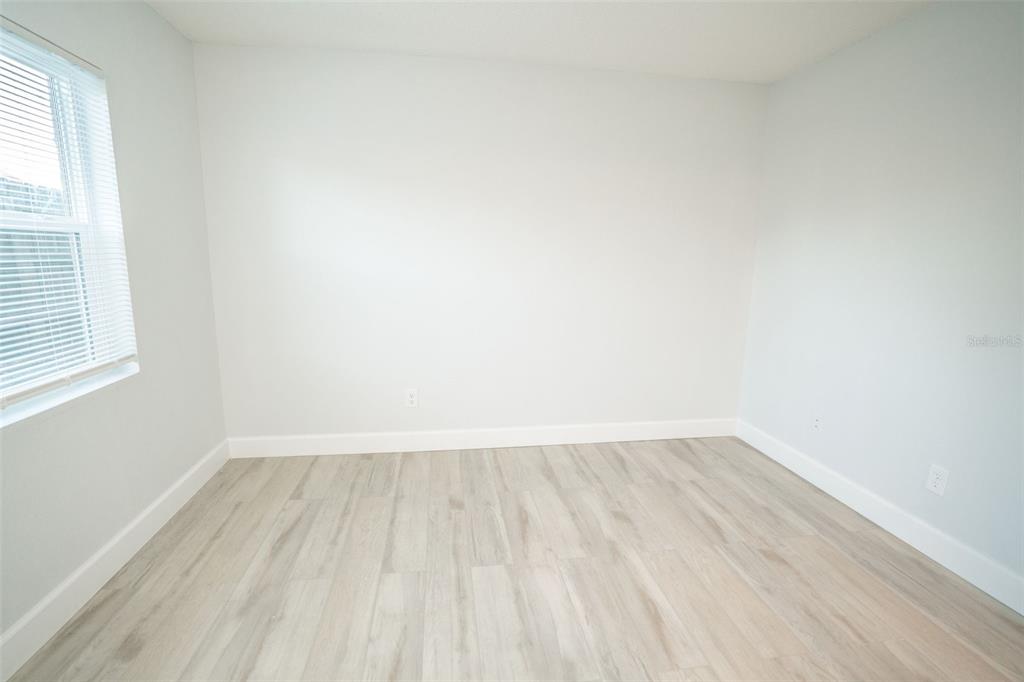 An empty room features light-colored wood-look flooring, white walls, and a window with blinds — 11312 N 52ND STREET UNIT A11, TAMPA, FL