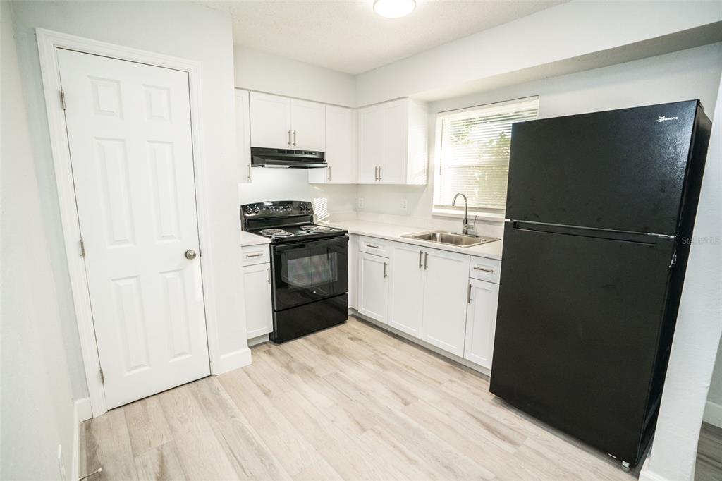 A kitchen features white cabinets, black appliances, and light wood-look flooring — 11312 N 52ND STREET UNIT A11, TAMPA, FL