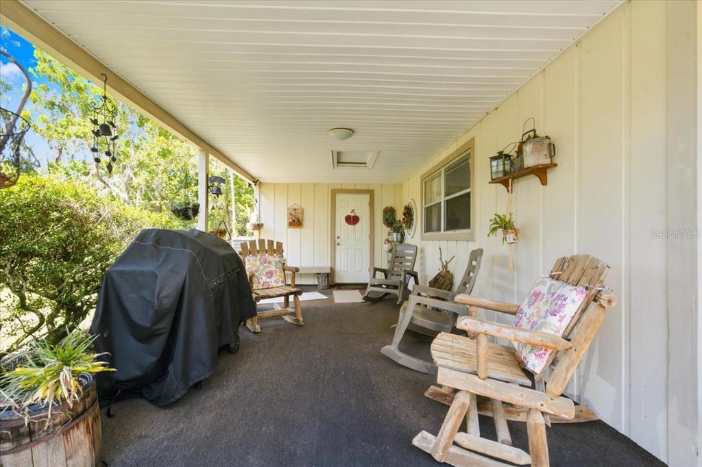 A covered porch features a concrete floor, several wooden rocking chairs, and a covered grill — 15535 RENEE LANE, HUDSON, FL