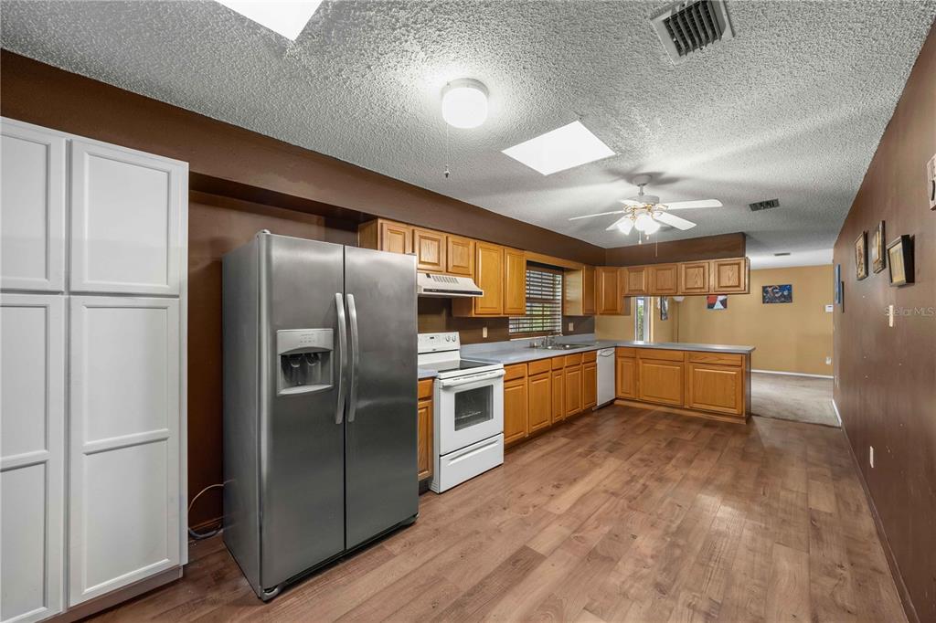 A kitchen features wood cabinets, stainless steel appliances, and wood-look flooring under a textured ceiling — 4950 NE 23RD AVENUE, OCALA, FL