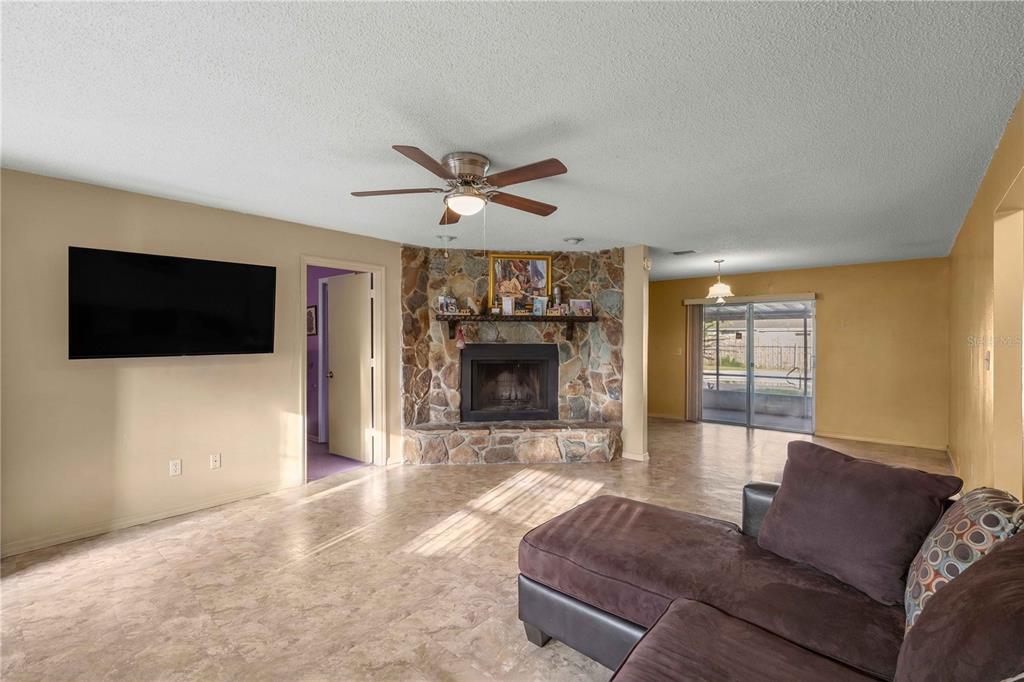 A living room features a corner stone fireplace, a ceiling fan, and tile flooring — 4950 NE 23RD AVENUE, OCALA, FL