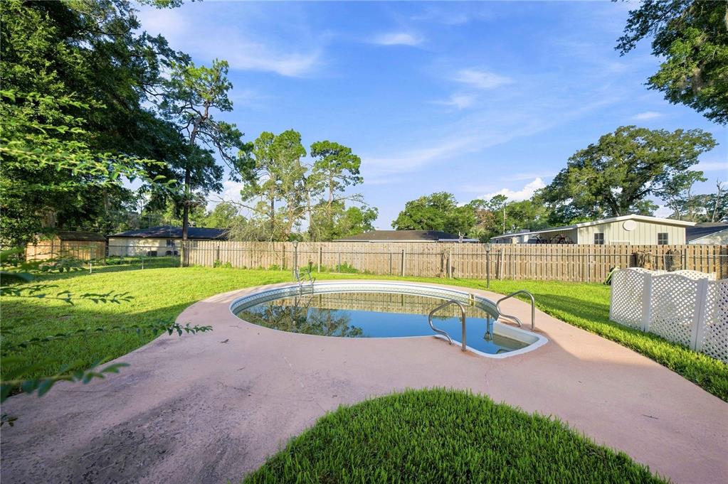 A backyard features a circular above-ground pool set into a concrete patio with grass — 4950 NE 23RD AVENUE, OCALA, FL