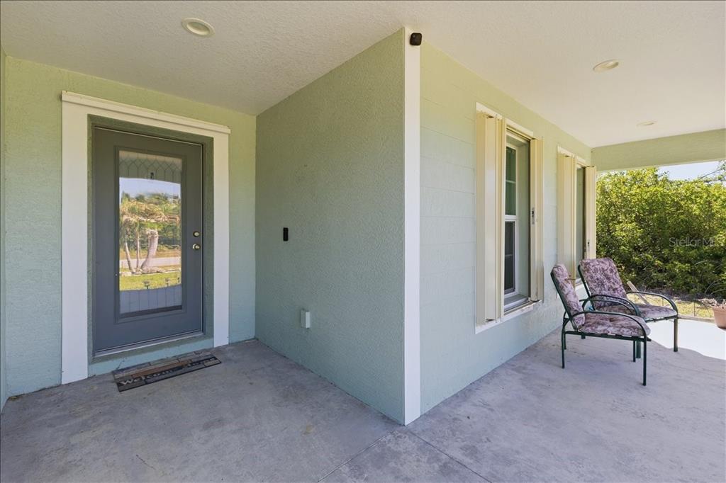 A light green covered porch features a gray front door and two outdoor chairs — 138 SUNNY WAY, ROTONDA WEST, FL