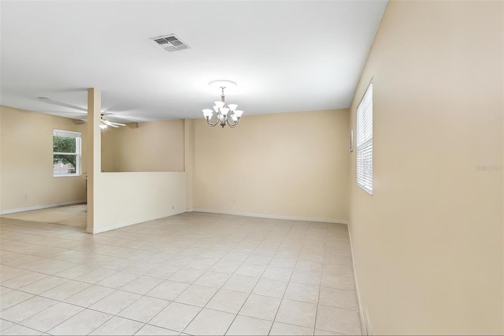 A spacious room with beige walls, tile flooring, a chandelier, and a partial wall divider — 1585 AUBURN HILLS COURT, TAVARES, FL