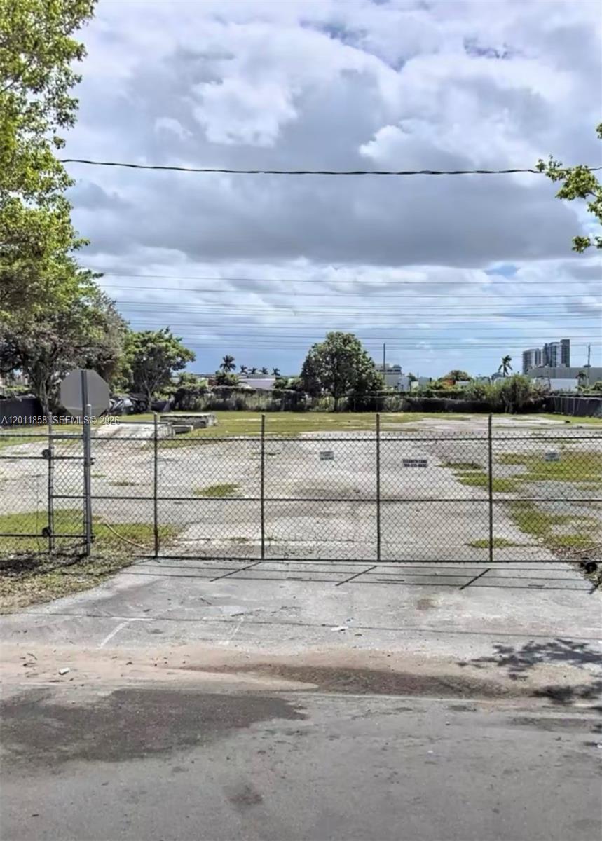 A fenced, vacant concrete lot sits under a cloudy sky with trees in the background — 8322 NW 64, Miami FL 33166, MIAMI, FL