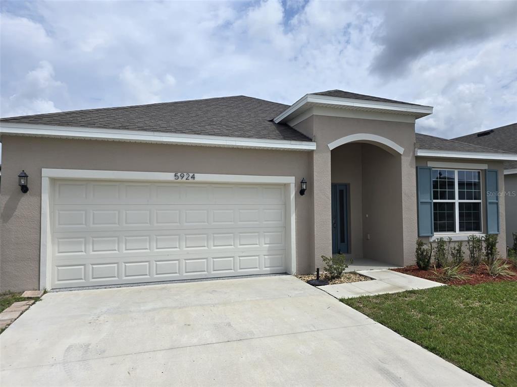 A single-story house with a beige stucco exterior, a two-car garage, and blue window shutters — 5924 CATAMARAN AVENUE, HAINES CITY, FL