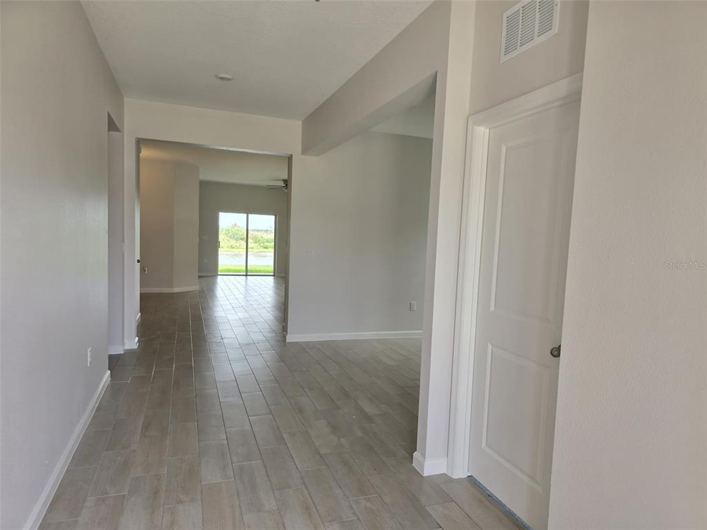 A hallway with light-colored tile flooring leads toward a living area with sliding glass doors — 5924 CATAMARAN AVENUE, HAINES CITY, FL