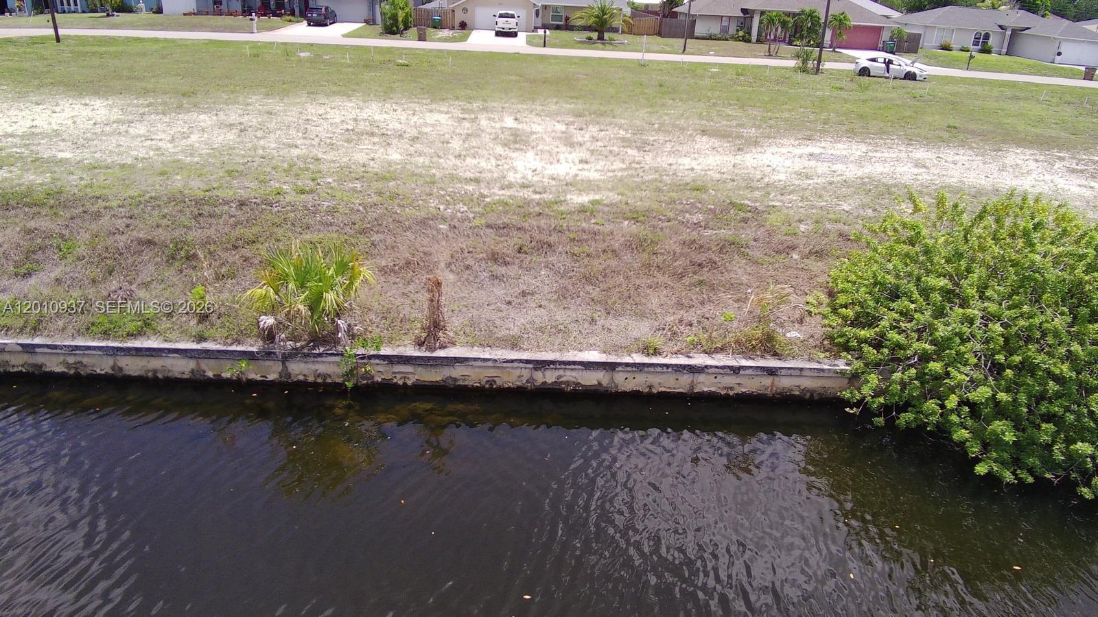 An aerial view shows a vacant waterfront lot with a concrete seawall and nearby houses — 1020 SE 13th Ave, Cape Coral FL 33990, CAPE CORAL, FL
