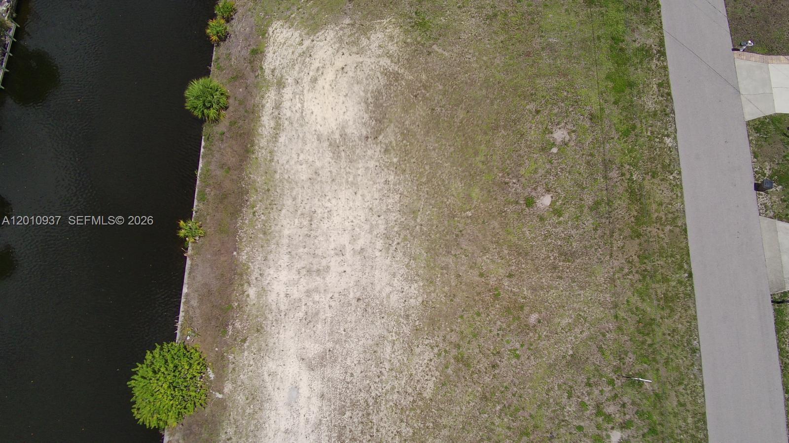 An aerial view shows a vacant, grassy waterfront lot next to a paved road — 1020 SE 13th Ave, Cape Coral FL 33990, CAPE CORAL, FL