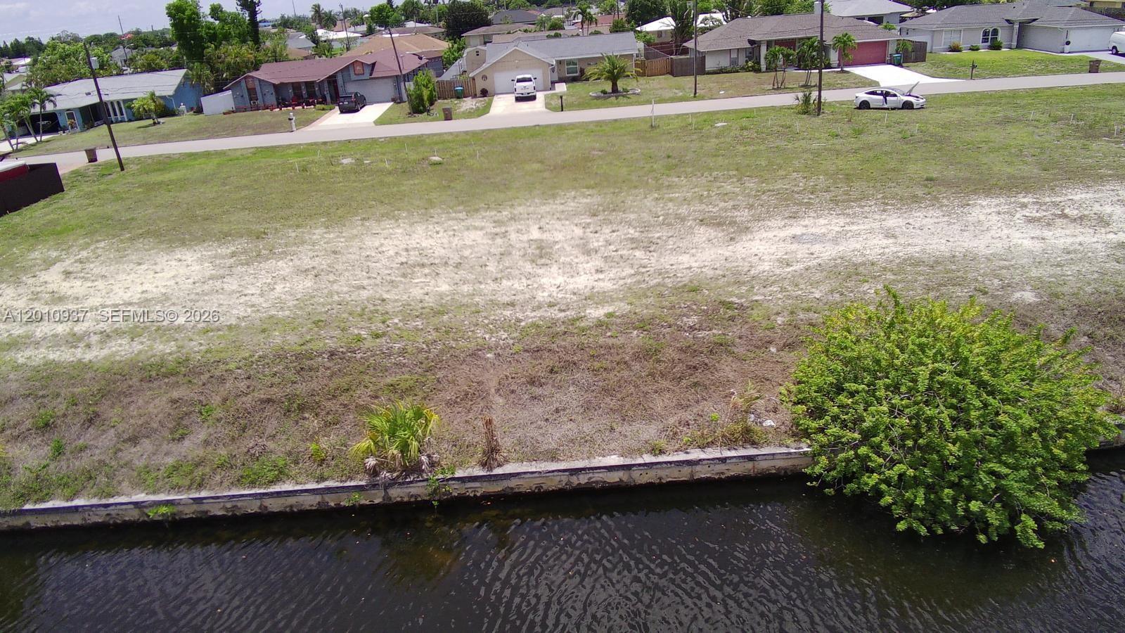 An aerial view of a vacant waterfront lot with a concrete seawall and nearby houses — 1020 SE 13th Ave, Cape Coral FL 33990, CAPE CORAL, FL