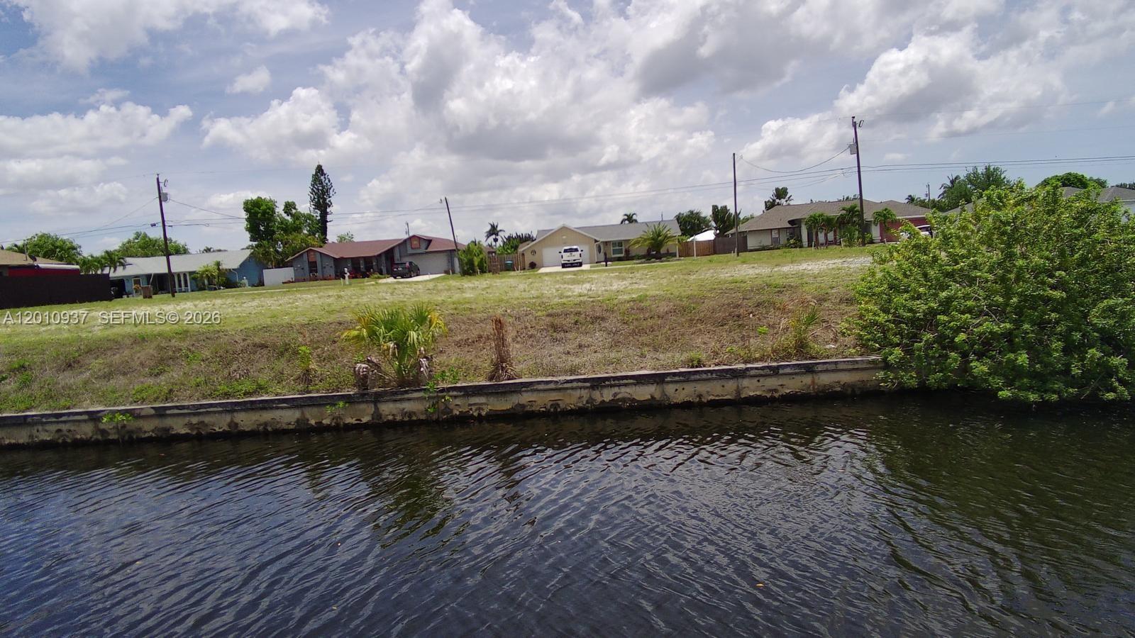 A view of a canal with a concrete seawall in front of a grassy lot — 1020 SE 13th Ave, Cape Coral FL 33990, CAPE CORAL, FL