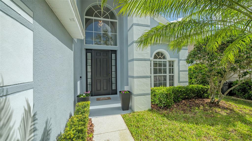 The exterior of a house features a dark front door, arched windows, and a palm tree — 6433 BLUE GROSBEAK CIRCLE, LAKEWOOD RANCH, FL