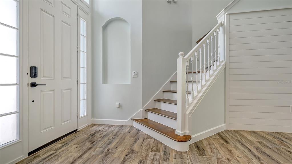 An entryway features wood-look flooring, a white front door, a wall niche, and a staircase — 6433 BLUE GROSBEAK CIRCLE, LAKEWOOD RANCH, FL