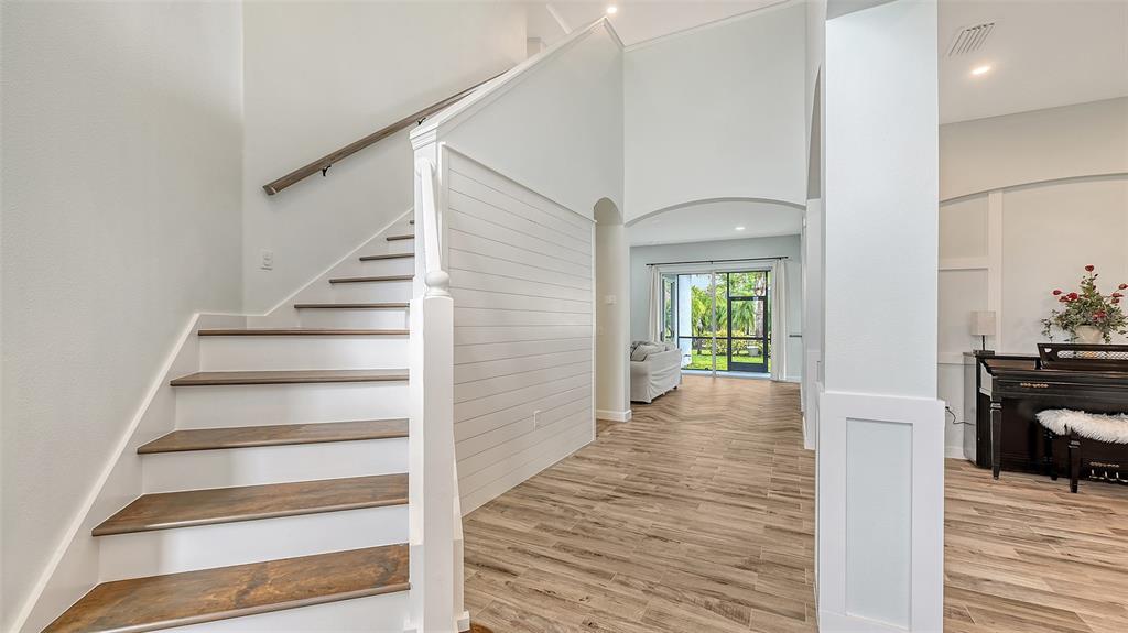 A foyer features a staircase with wood treads, shiplap wall paneling, and wood-look tile flooring — 6433 BLUE GROSBEAK CIRCLE, LAKEWOOD RANCH, FL