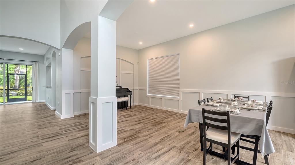 A dining room with wood-look tile flooring, white wainscoting, and a piano in the background — 6433 BLUE GROSBEAK CIRCLE, LAKEWOOD RANCH, FL