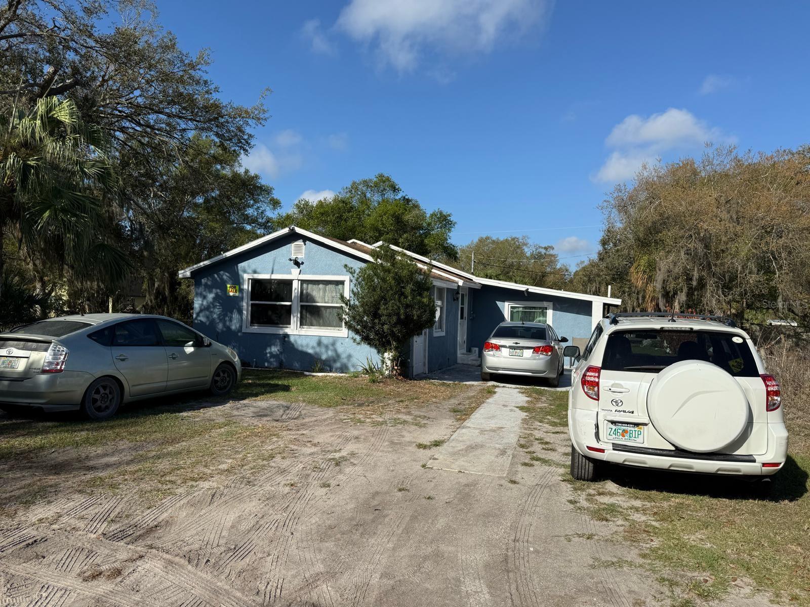 A blue single-story house with a dirt driveway and three parked cars in front — 414 Spring Avenue, FL 34266, FL