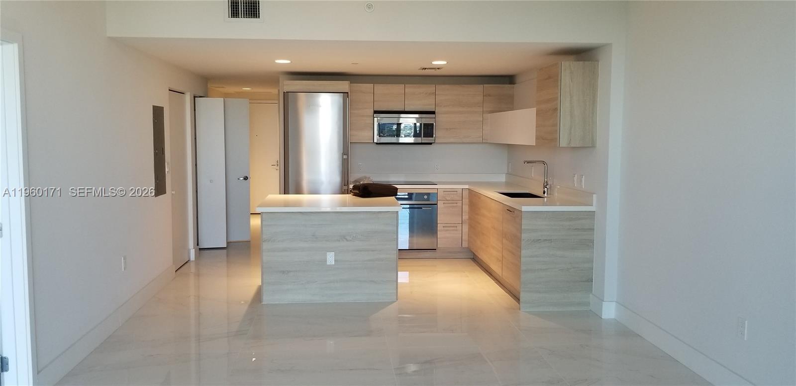 A modern kitchen features light wood cabinets, stainless steel appliances, and white countertops — 16385 Biscayne Blvd # 1516, Miami FL 33160, MIAMI, FL