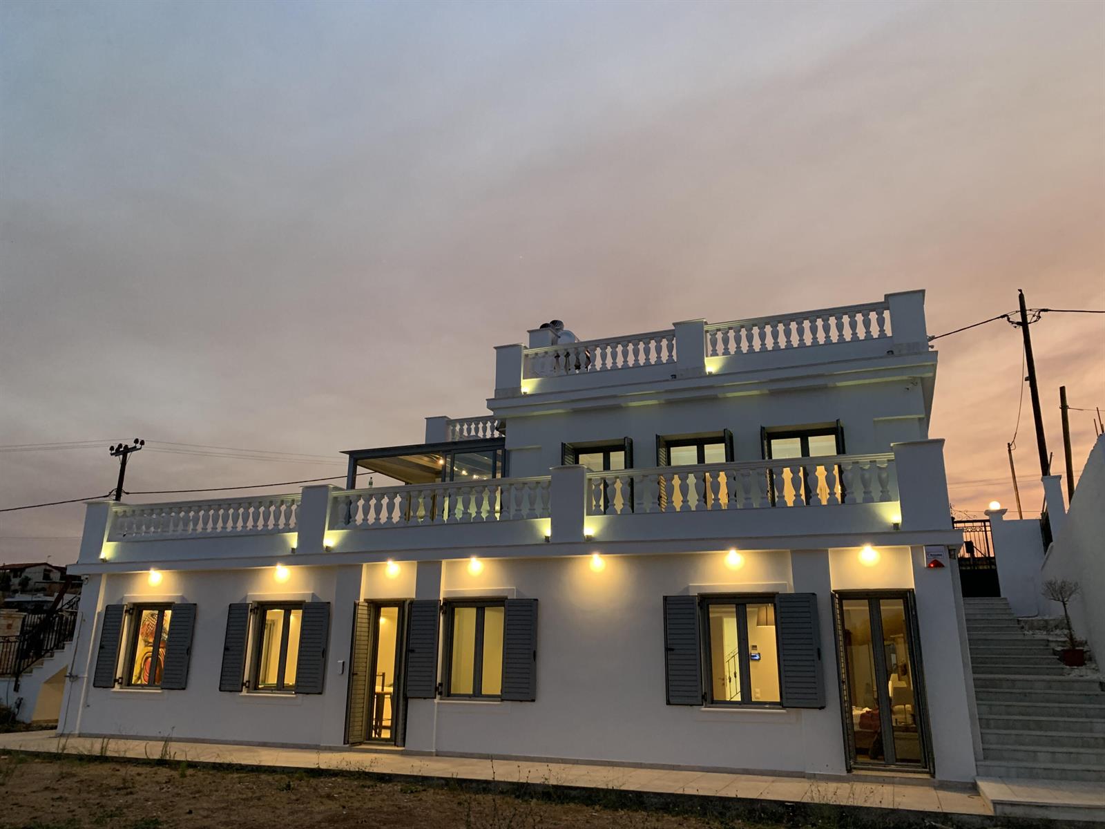 A two-story white house with a balcony, balustrades, and exterior lighting at dusk — 23 Zefirou, Rafina, Greece, FL
