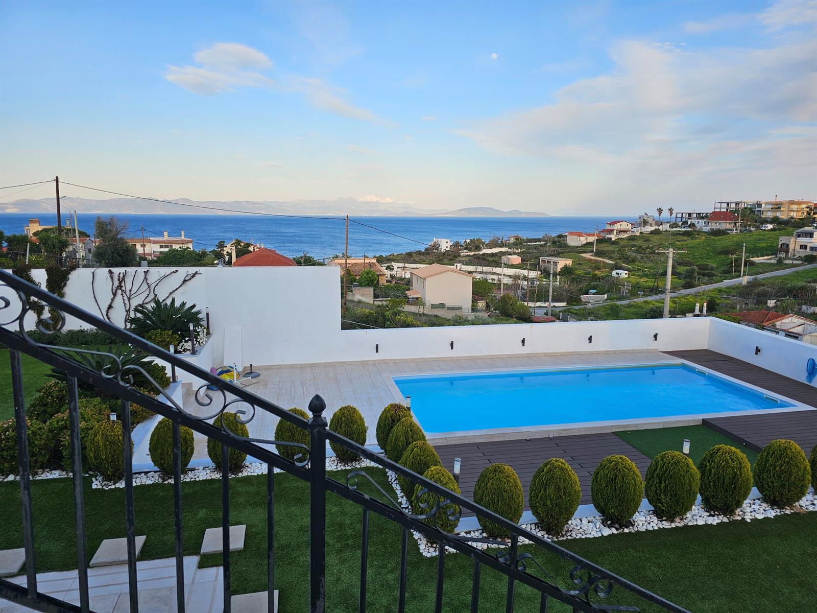 An outdoor swimming pool with a deck and lawn overlooks the sea and distant mountains — 23 Zefirou, Rafina, Greece, FL