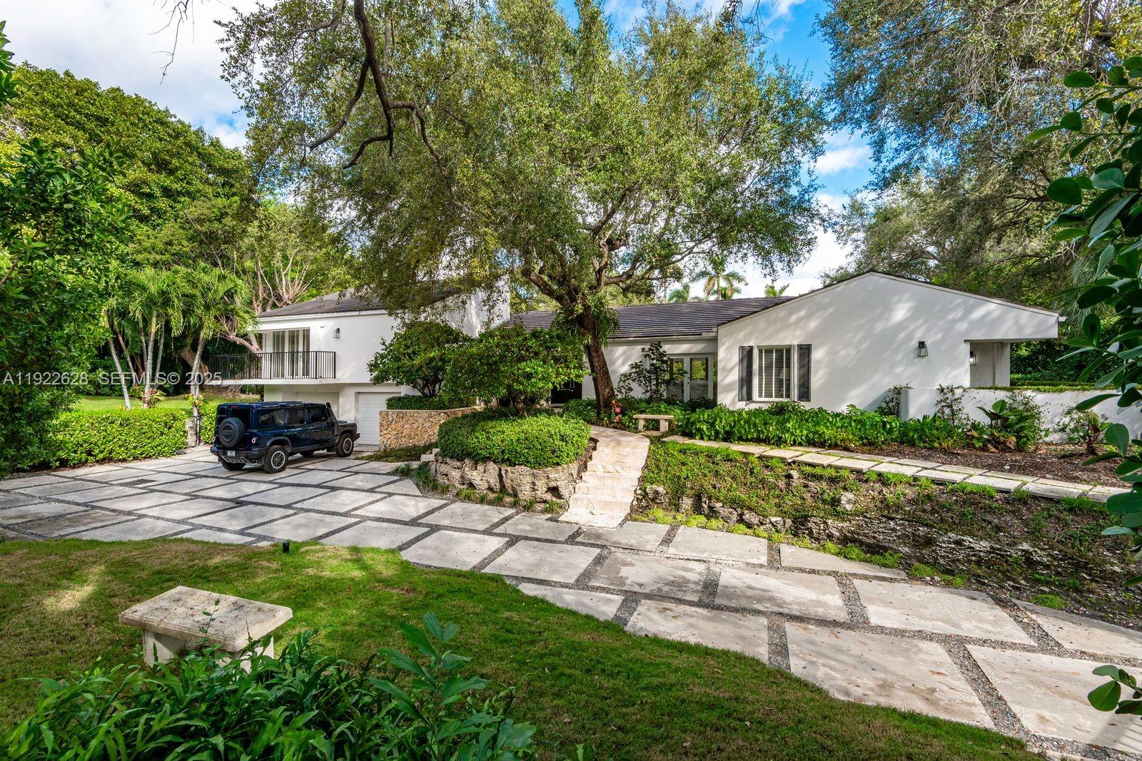 A two-story white house with a paved driveway and a large tree in the front yard — 7000 Robles St, Coral Gables FL 33143, CORAL GABLES, FL