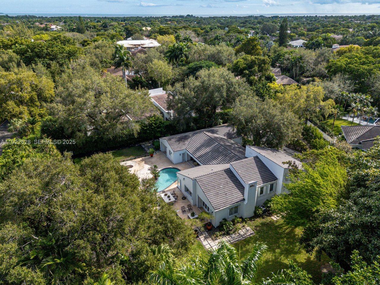 An aerial view shows a single-story house with a swimming pool surrounded by lush trees — 7000 Robles St, Coral Gables FL 33143, CORAL GABLES, FL