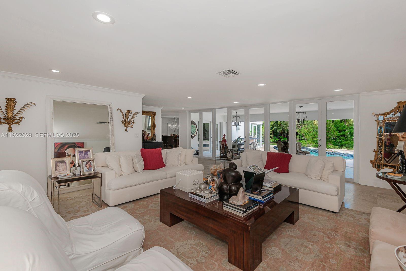 A living room features white sofas, a large wooden coffee table, and floor-to-ceiling glass doors — 7000 Robles St, Coral Gables FL 33143, CORAL GABLES, FL