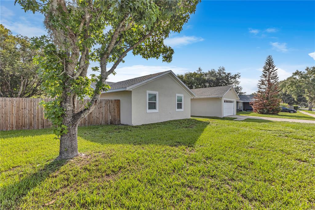 A side view of a beige house with a wooden fence and a large tree — 4901 REGINALD ROAD, ORLANDO, FL