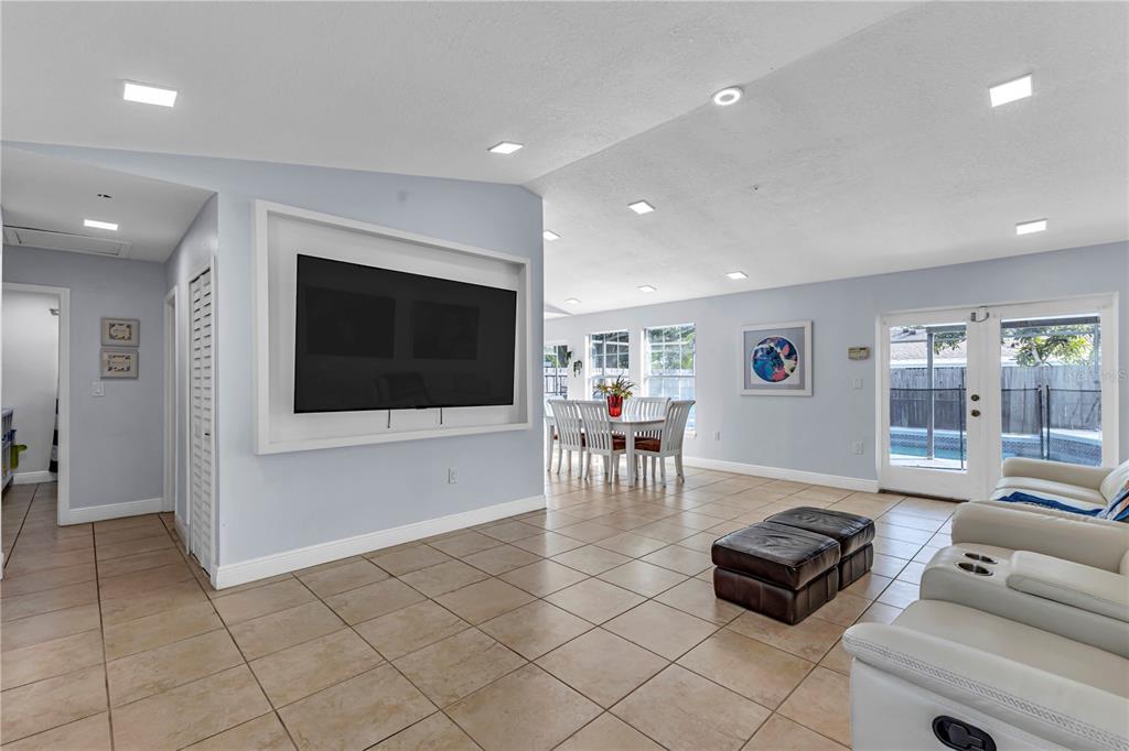A living room features a wall-mounted television, tile flooring, and a dining area beyond — 4901 REGINALD ROAD, ORLANDO, FL