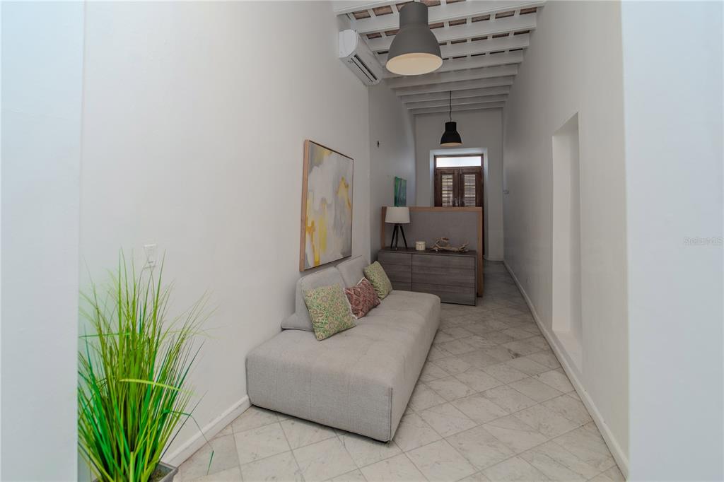 A narrow living area features a gray sofa, tiled floors, and exposed ceiling beams — 152 SOL STREET, OLD SAN JUAN, PR
