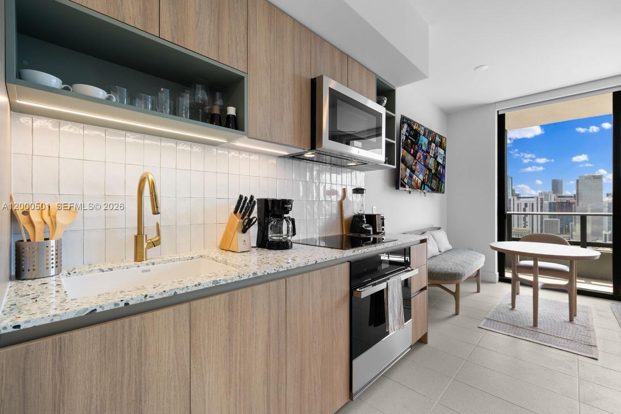 A modern kitchen features wood-toned cabinetry, a gold faucet, and a view of city skyscrapers — 159 NE 6 ST ST # 3206, Miami FL 33132, MIAMI, FL