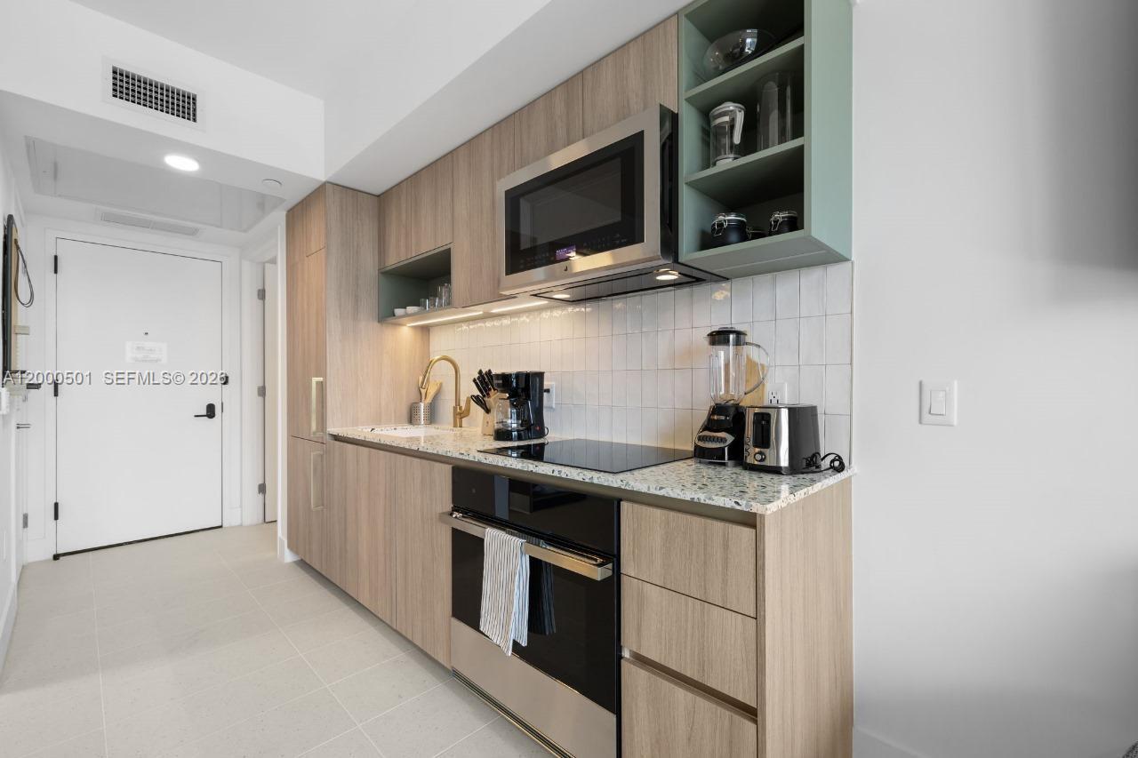 A modern kitchen features light wood cabinets, a speckled countertop, and a built-in microwave — 159 NE 6 ST ST # 3206, Miami FL 33132, MIAMI, FL