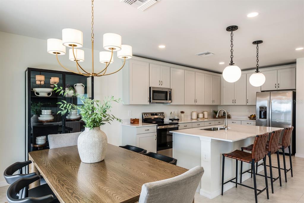 A kitchen and dining area with light cabinets, a center island, and a wooden table — 9617 VIBRANT LANE, VENICE, FL