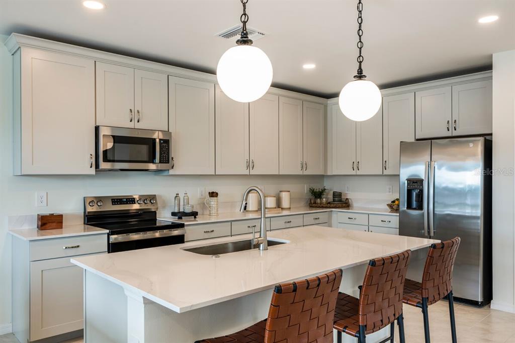 A modern kitchen features white cabinetry, stainless steel appliances, and a large quartz-topped island — 9617 VIBRANT LANE, VENICE, FL