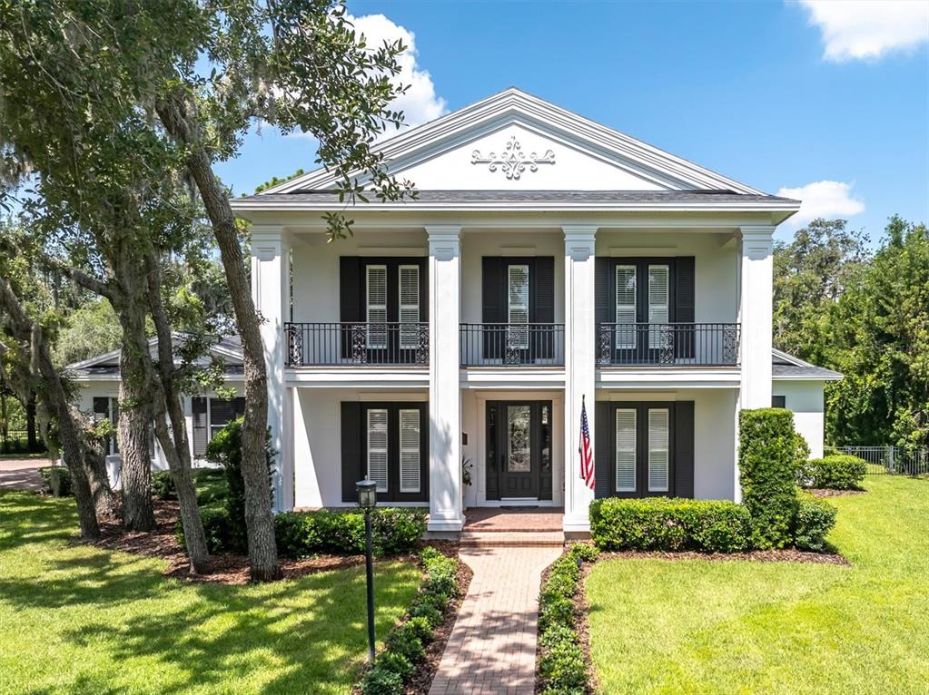 A two-story white house with a columned porch, balcony, and brick walkway — 16301 DUNLINDALE DRIVE, LITHIA, FL