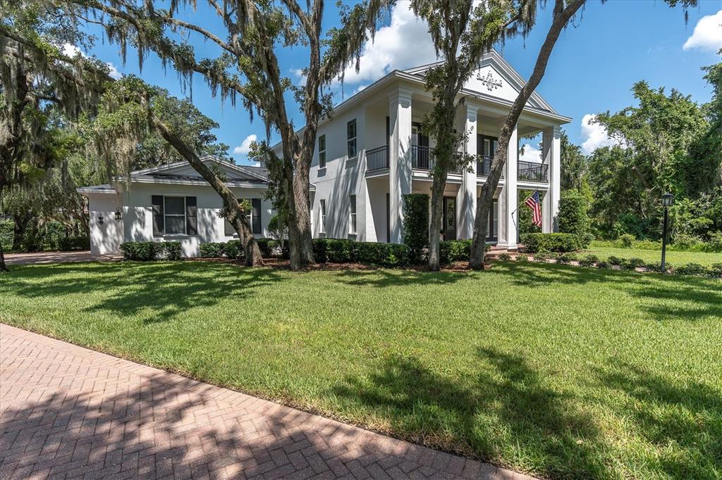 A two-story white house with a columned front porch stands behind a large green lawn — 16301 DUNLINDALE DRIVE, LITHIA, FL