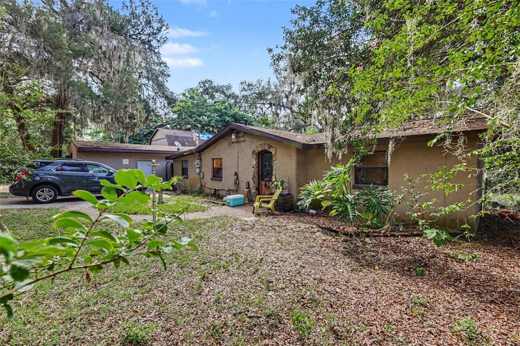 A single-story stucco house with a dark roof sits behind a tree-filled yard — 13395 SE 106TH AVENUE, OCKLAWAHA, FL