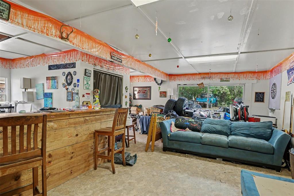 A rustic indoor bar area features a wooden counter, blue sofa, and concrete flooring — 13395 SE 106TH AVENUE, OCKLAWAHA, FL
