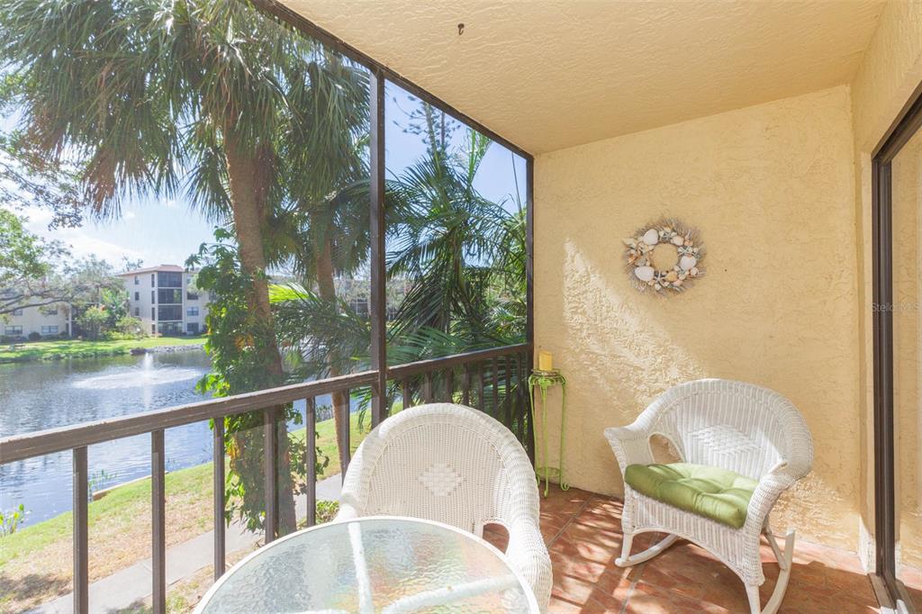 A screened-in balcony with wicker chairs, a glass table, and a view of a pond — 315 30TH AVENUE W UNIT B201, BRADENTON, FL