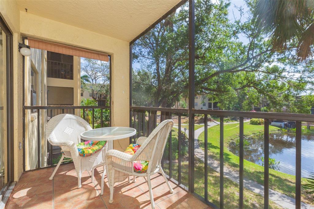 A screened-in balcony features two wicker chairs, a glass-top table, and a view of a pond — 315 30TH AVENUE W UNIT B201, BRADENTON, FL