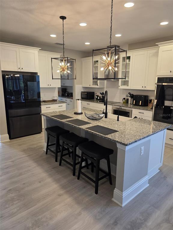 A modern kitchen features white cabinetry, granite countertops, a central island with stools, and pendant lighting — 7520 GREENHEART COURT, WESLEY CHAPEL, FL