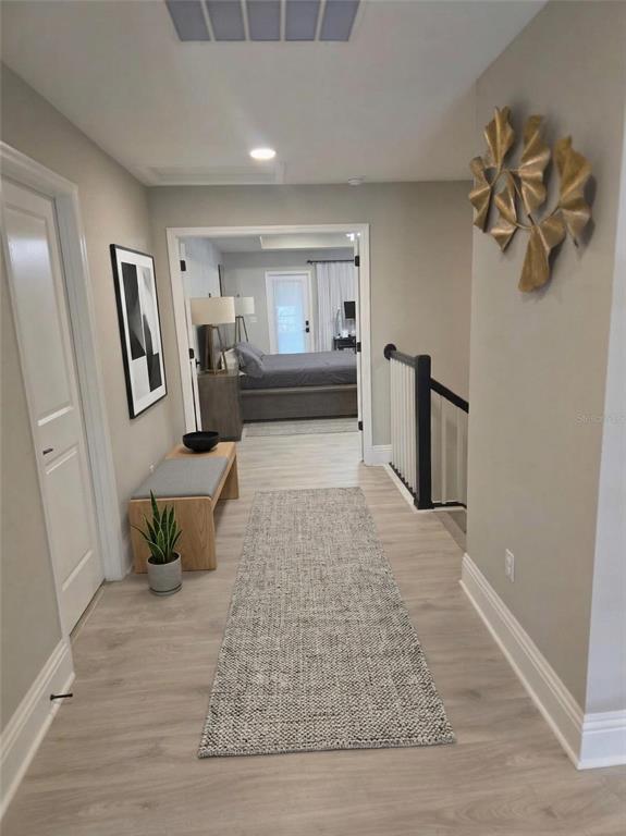 A hallway with light wood flooring leads to a bedroom through double doors — 7520 GREENHEART COURT, WESLEY CHAPEL, FL