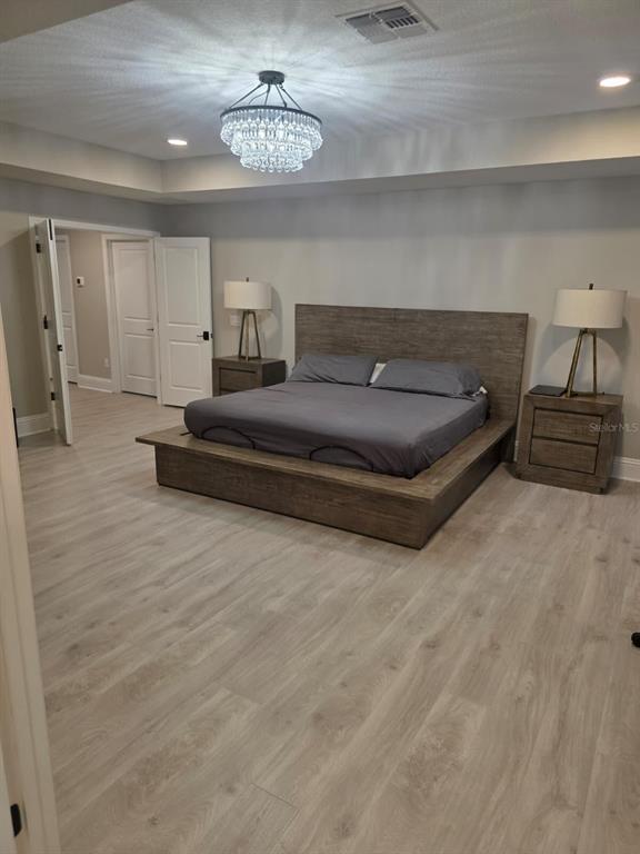 A bedroom features a wooden platform bed, two matching nightstands, and a crystal chandelier — 7520 GREENHEART COURT, WESLEY CHAPEL, FL