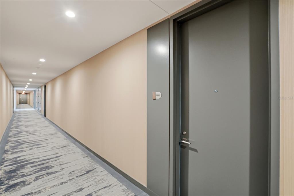A long apartment hallway features a gray door, beige walls, and patterned carpet flooring — 400 CENTRAL AVENUE UNIT 2008, ST PETERSBURG, FL