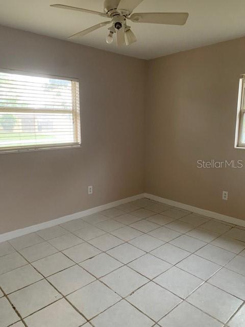 An empty bedroom features light-colored tile flooring, beige walls, a ceiling fan, and two windows — 1940 64TH AVENUE N, ST PETERSBURG, FL