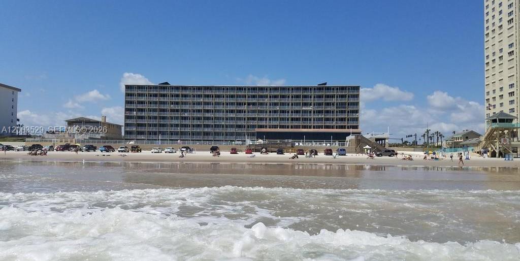 A multi-story beachfront condominium building stands behind a sandy beach with parked cars — 3501 S ATLANTIC AVE # G140, Daytona FL 32118, DAYTONA, FL