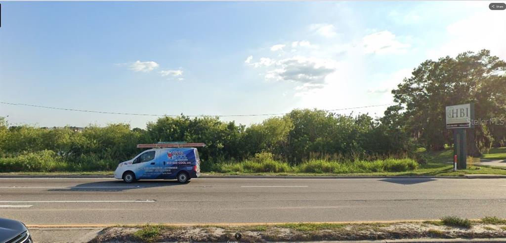 A blue and white service van drives along a road in front of a vacant lot — HWY 60 E, LAKE WALES, FL