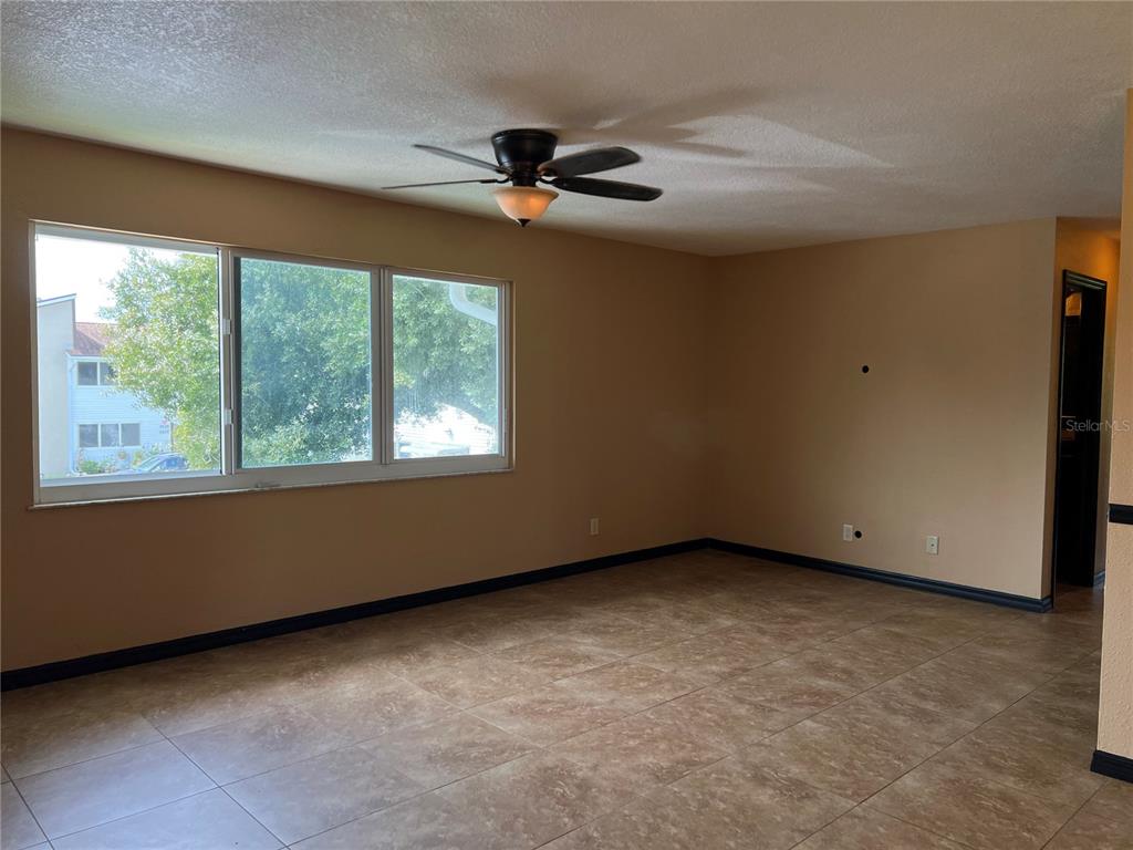 An empty room features tan walls, dark baseboards, tile flooring, and a ceiling fan — 22481 WESTCHESTER BOULEVARD UNIT B27, PUNTA GORDA, FL