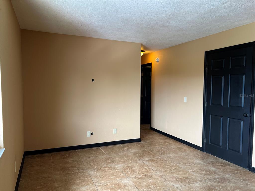 An empty room features tan walls, dark trim, a black door, and tiled flooring — 22481 WESTCHESTER BOULEVARD UNIT B27, PUNTA GORDA, FL